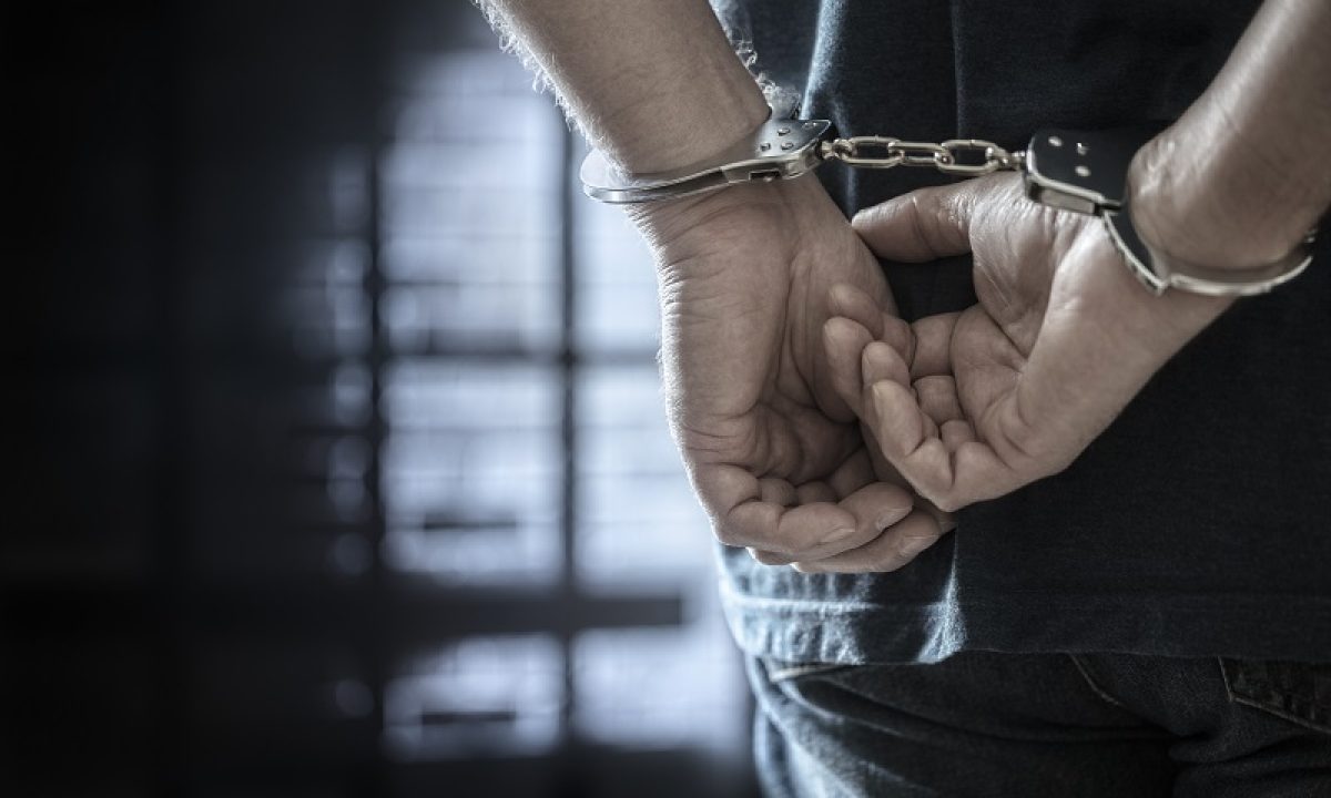 Arrested man in handcuffs with handcuffed hands behind back in prison